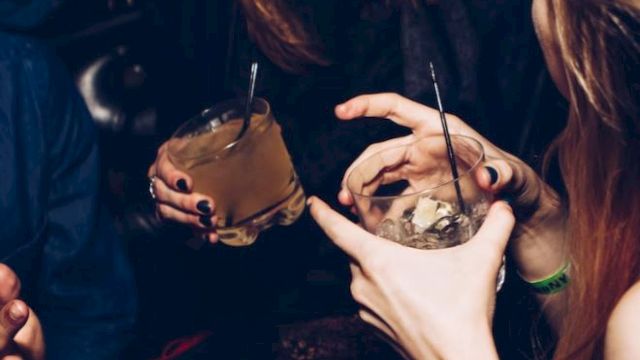 People enjoying drinks and conversation at a social gathering, holding cocktails and laughing.