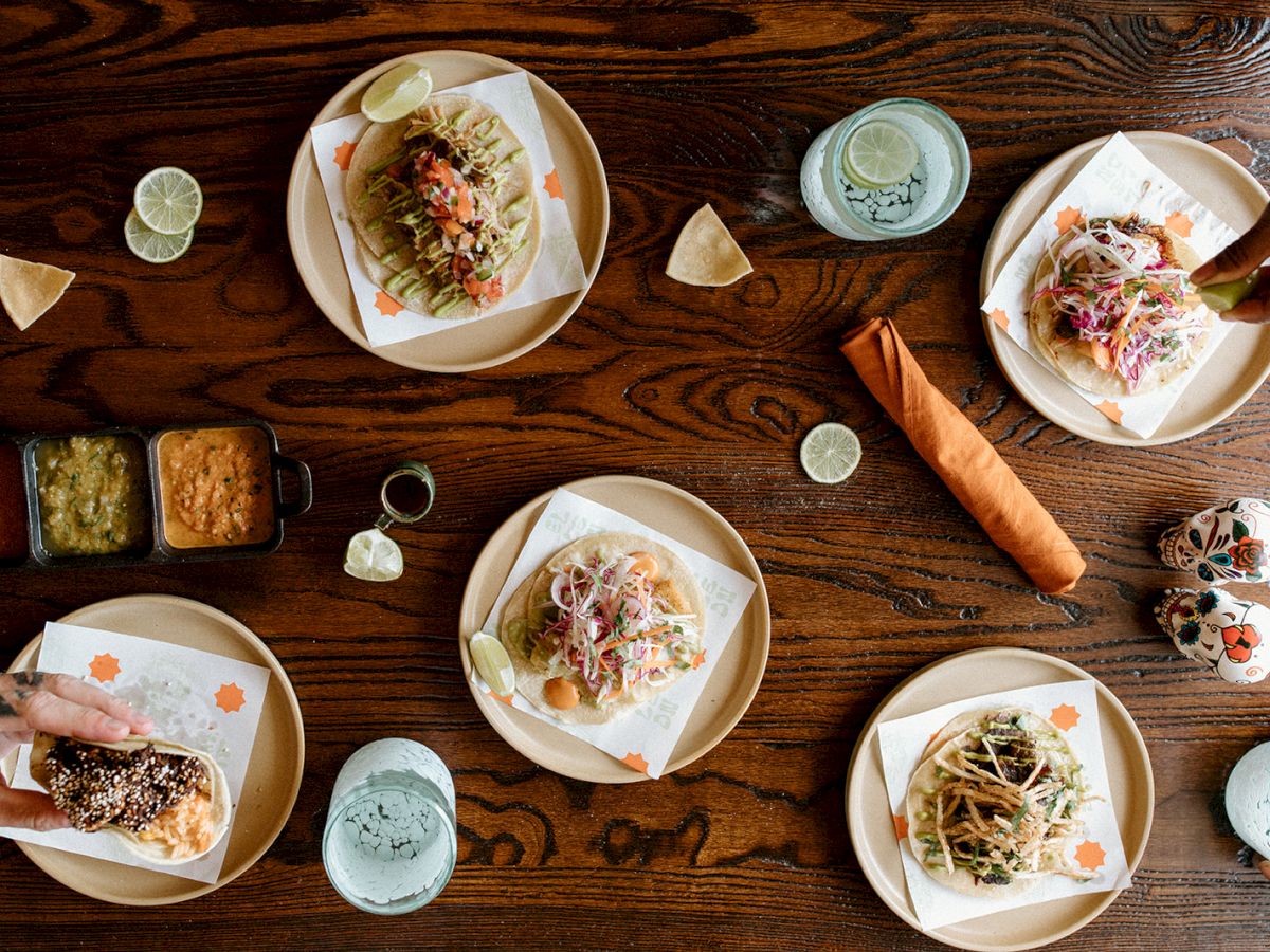 A table with arranged tacos, condiments, drinks, and decorative skulls, viewed from above.