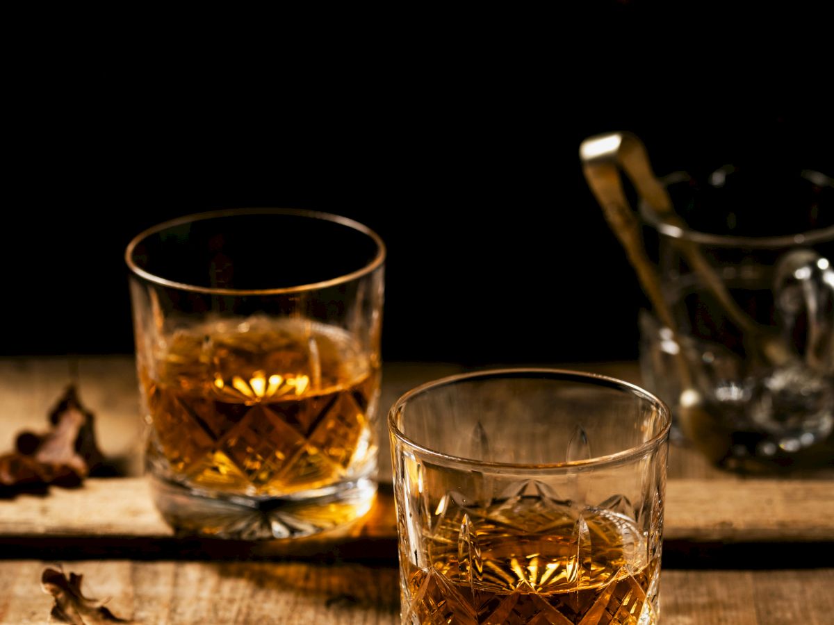 Two glasses of whiskey on a wooden table, with scattered autumn leaves around, creating a warm and cozy atmosphere.