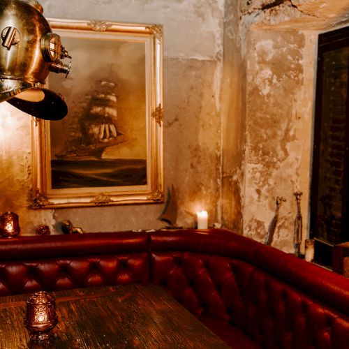 The image shows a room with vintage decor, including a red leather booth, a nautical painting, and a diving helmet light fixture.