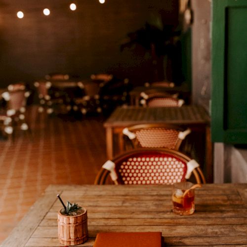 A cozy café setting with wooden tables, rattan chairs, a menu, drink, and dim string lights creating a warm atmosphere.