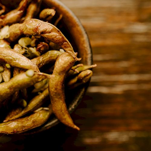 A bowl of roasted edamame pods placed on a wooden surface, creating a warm and rustic ambiance.