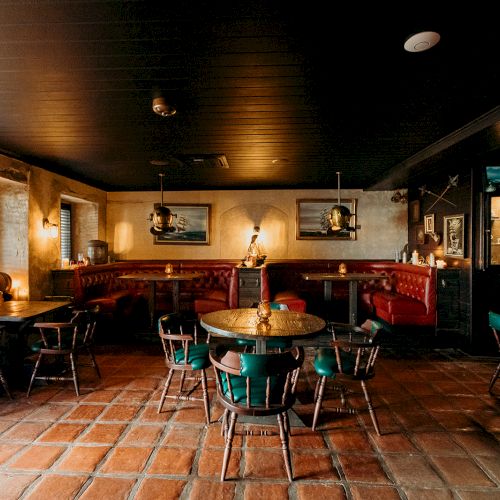 A cozy restaurant interior with brick flooring, wooden chairs, red booths, ambient lighting, and framed artwork on the walls.