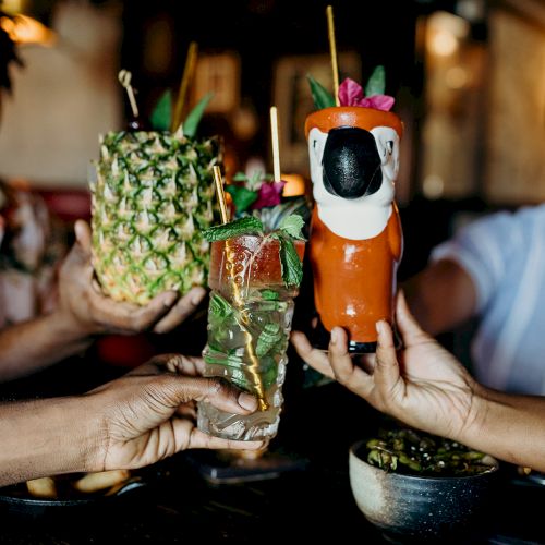 People toasting with colorful tropical drinks in unique glasses.