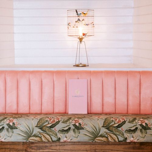 A pink and floral bench with a menu, topped by a decorative lamp, surrounded by tropical wallpaper.