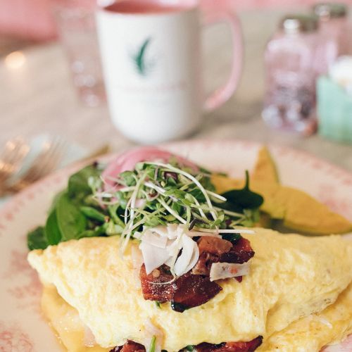 A stuffed omelette with greens and a mug in the background, set on a floral plate, creating a cozy breakfast scene.