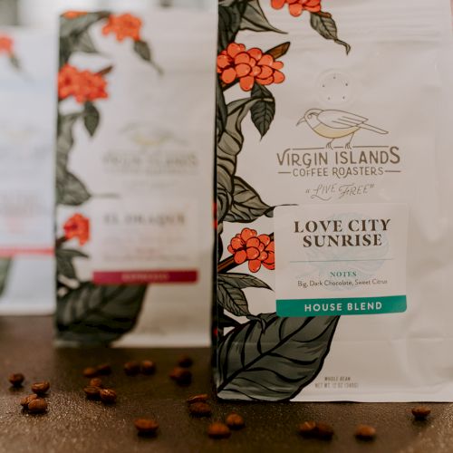 The image shows packages of Virgin Islands Coffee Roasters' "Love City Sunrise" house blend, with coffee beans scattered around.