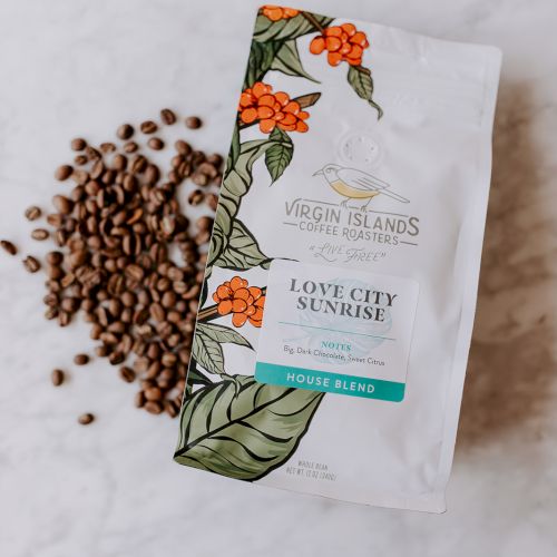 A bag of "Love City Sunrise" coffee blend from Virgin Islands Coffee Roasters is next to a pile of coffee beans on a marble surface.