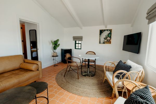 A cozy living room with a brown couch, wicker chairs, table, TV, and decor on terracotta tile flooring.