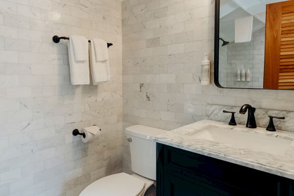 A modern bathroom with a toilet, marble countertop, black vanity, mirror, towel rack, and decorative floor tiles.