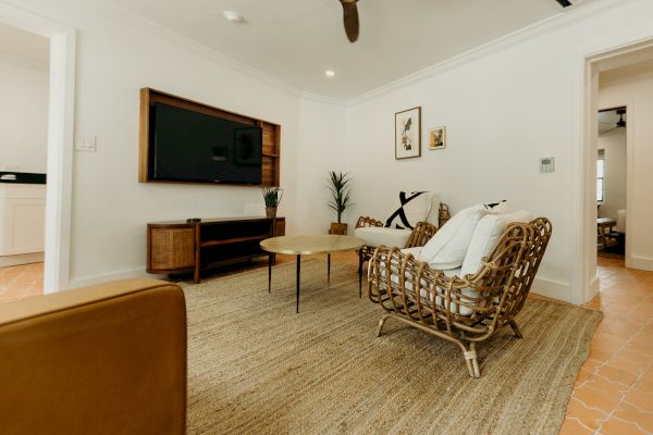 A cozy living room with wicker chairs, a round coffee table, a TV on the wall, and decor, featuring a neutral color scheme and woven rug.