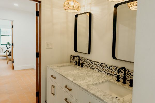 A bathroom features patterned floor tiles, a double vanity with marble countertops, black fixtures, and pendant lights.