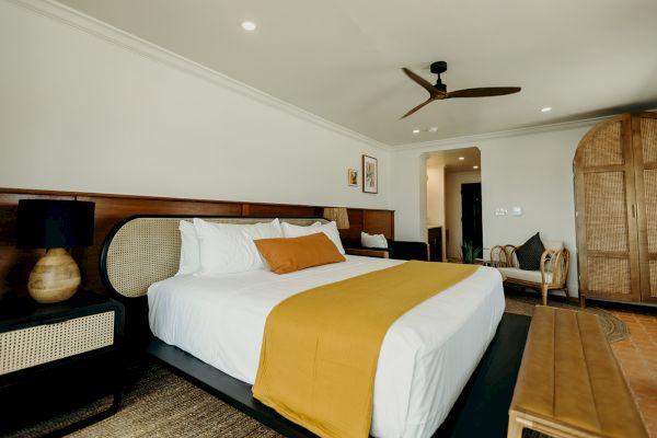 A modern bedroom with a large bed, yellow accents, wooden furniture, and ceiling fan. Cozy and inviting atmosphere.