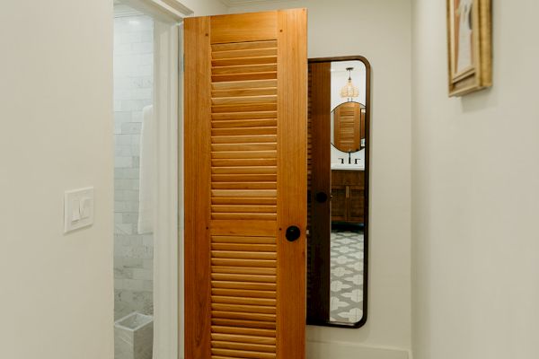 A small hallway with patterned floor tiles leads to a room with a wooden sliding door. A mirror and a framed picture are on the walls.