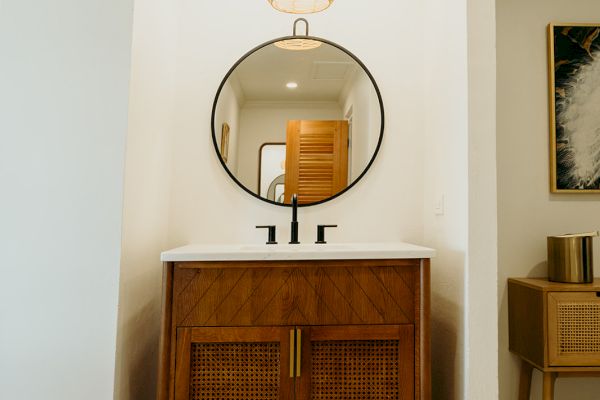 The image shows a bathroom vanity with a round mirror and a wooden cabinet, under a pendant light, on patterned tile flooring.