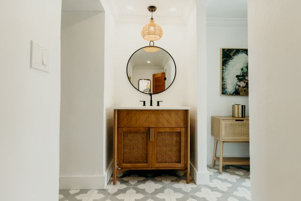 A stylish bathroom featuring a wooden vanity with a round mirror, geometric floor tiles, and modern lighting.