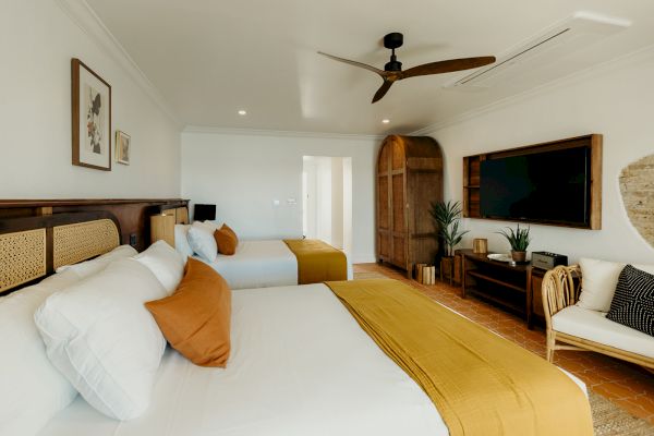 A modern bedroom with two beds, a TV, wooden furniture, plants, and decorative elements in a light and airy setting.