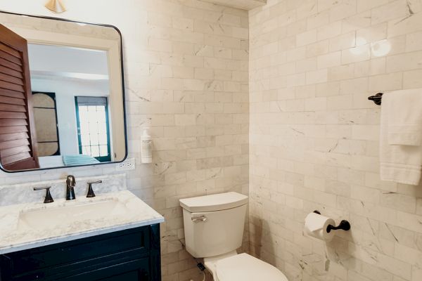 The image shows a bathroom with a toilet, a vanity with a mirror, a towel rack, and ornate floor tiles.