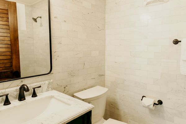 A bathroom with a toilet, a black vanity with a sink, a mirror, and patterned floor tiles. The walls are light-colored tiles.