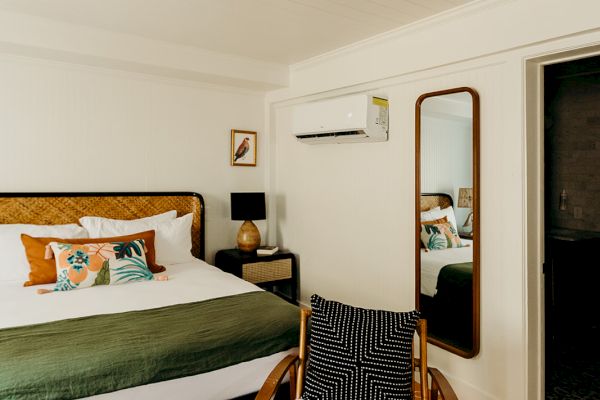 A cozy bedroom with a bed, decorative pillows, a wooden chair, a mirror, and an air conditioner on the wall.