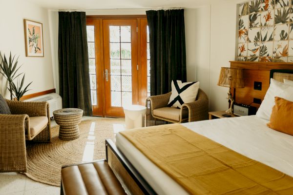 A cozy room with a double bed, wicker chairs, a round table, and a patterned accent wall. French doors open to the outside.